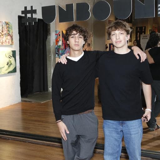 Two boys posing arm in arm beneath hashtag UNBOUND sign in gallery entrance.