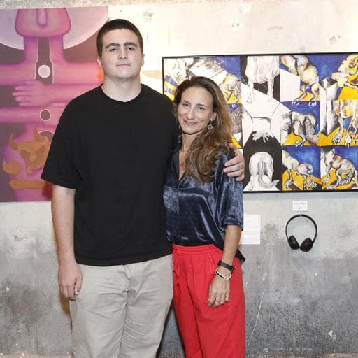 Young man and woman posing together before colorful paintings and headphones in gallery.