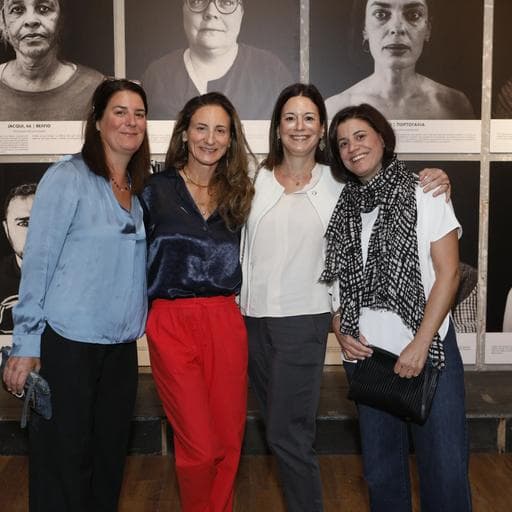 Four smiling women posing together in front of large black-and-white portrait photographs.