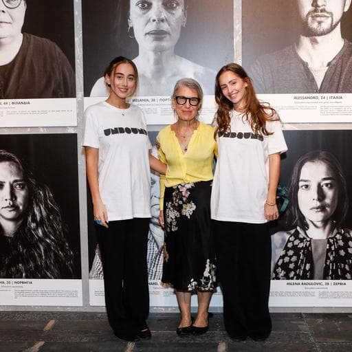 Three women, two in UNBOUND shirts, posing before wall of black-and-white portraits.