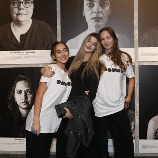 Three young women posing together before wall of black-and-white portrait photographs.