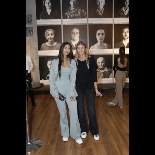Two young women standing before a wall of large black-and-white portrait photographs.