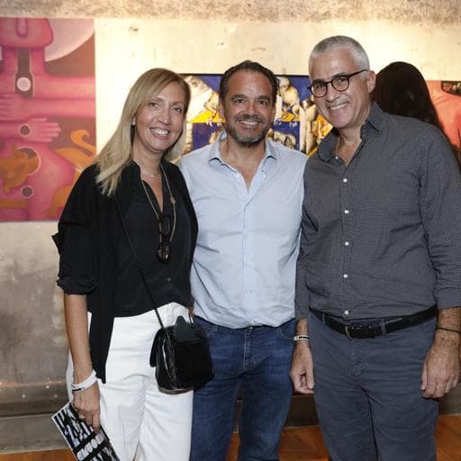 Three smiling visitors posing together with colorful abstract paintings behind them in gallery.