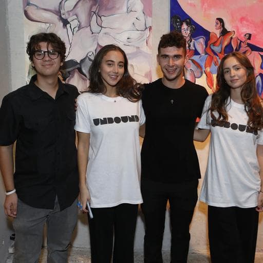 Four young people posing, two in UNBOUND t-shirts, before pink and blue figurative paintings.