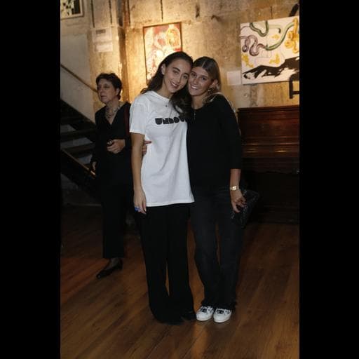 Two women embracing in gallery with abstract paintings and piano behind them.