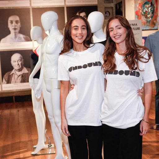 Two women in UNBOUND t-shirts posing beside white mannequins and portraits.