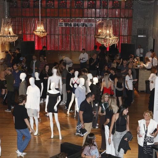 Crowd mingling among white mannequins under chandeliers beneath UNBOUND banner.