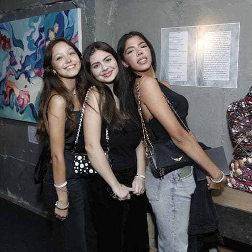 Three young women posing beside colorful abstract painting and wall text display.