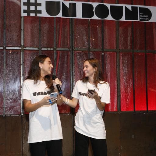 Two women in UNBOUND t-shirts speaking on stage under a hashtag UNBOUND banner.