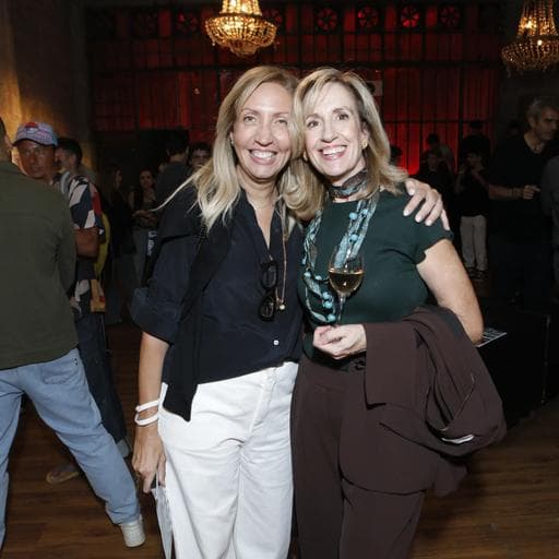 Two smiling blonde women embracing at crowded Unbound reception under chandeliers.