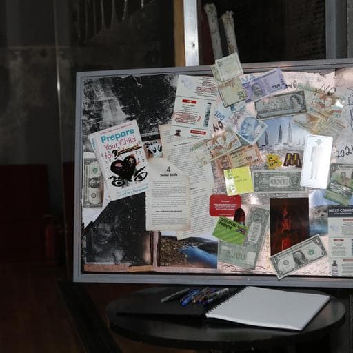 Collage artwork covered with banknotes, documents and pamphlets, with notebook below.