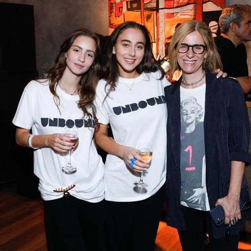 Three women posing with wine glasses, two wearing white UNBOUND t-shirts in gallery.