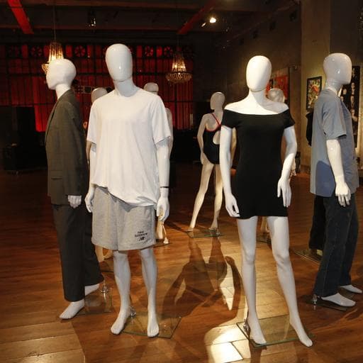 Clothing installation of white mannequins wearing casual outfits on wooden gallery floor.