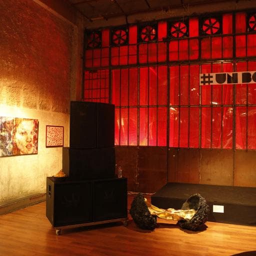 Gallery stage with red-lit windows, speakers, and partial hashtag UNBOUND sign above.