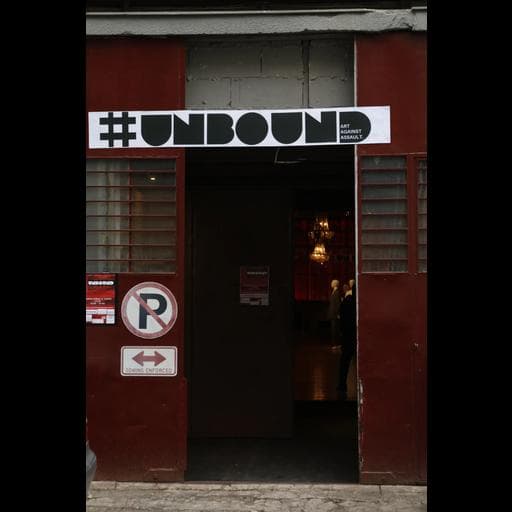 Entrance with red doors and white sign reading hashtag UNBOUND Art Against Assault.